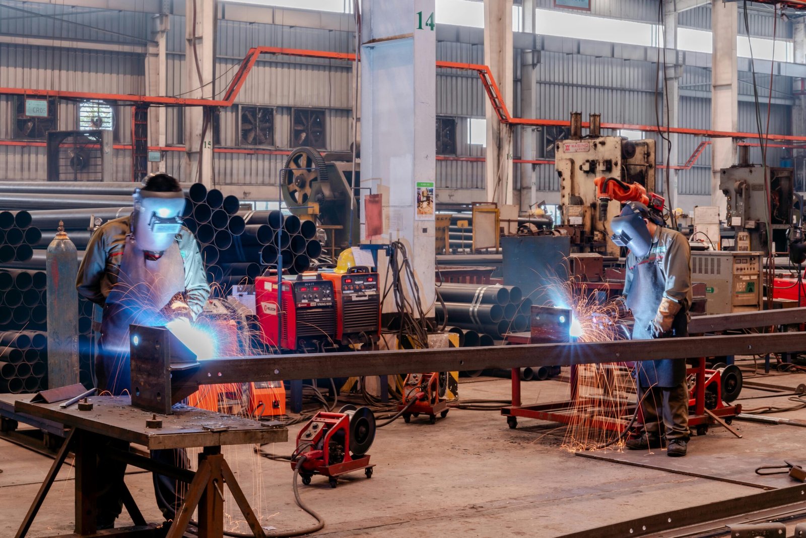 project-2 Two welders wearing protective gear working in a busy industrial factory workshop.